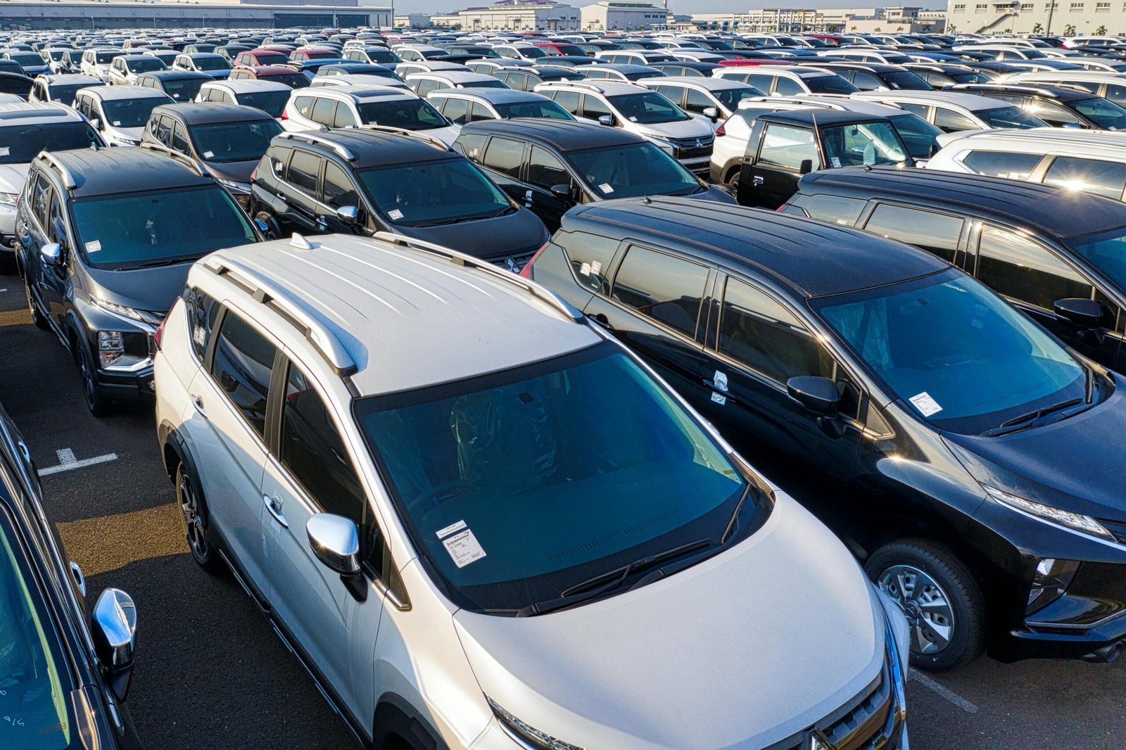 Modern sparkling clean new automobiles on asphalt parking near factory of manufacture in daytime